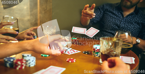 Image of Side view photo of friends sitting at wooden table. Friends having fun while playing board game.