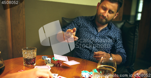 Image of Side view photo of friends sitting at wooden table. Friends having fun while playing board game.