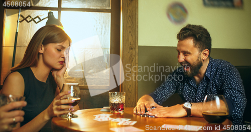 Image of Friends sitting at wooden table. Friends having fun while playing board game.