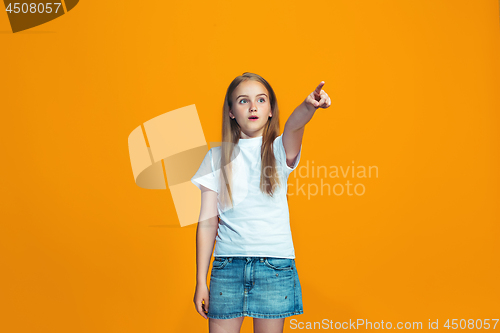 Image of The happy teen girl pointing to you, half length closeup portrait on orange background.
