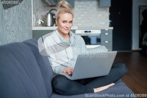 Image of Middle aged woman sitting on sofa in her living room and working on laptop