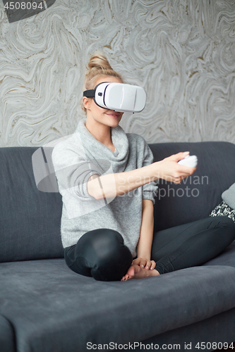 Image of Young woman watching videos or playing with VR glasses on head