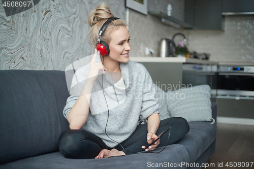 Image of Adorable middle aged blond woman sitting on sofa in her home and listen to the music