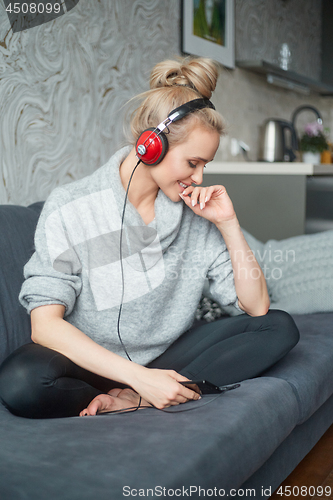 Image of Adorable middle aged blond woman sitting on sofa in her home and listen to the music