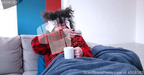 Image of sick man is holding a cup while sitting on couch