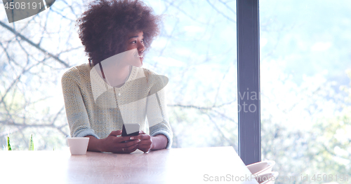 Image of black woman drinking coffee and using a mobile phone  at home