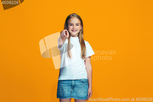 Image of The happy teen girl pointing to you, half length closeup portrait on orange background.