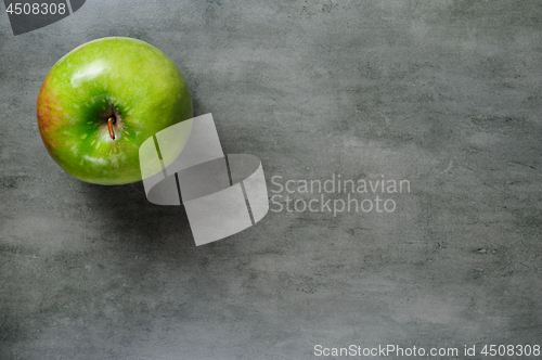 Image of one green apple on dark stone background, top view.