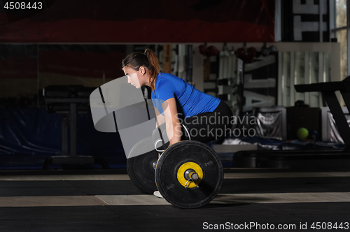 Image of Young woman doing deadlift workout with heavy barbell in dark gym