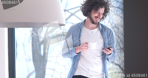 Image of young man drinking coffee and using a mobile phone  at home