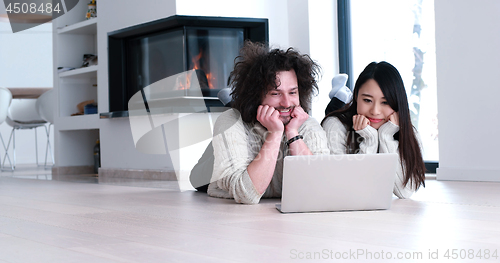 Image of young multiethnic couple using a laptop on the floor