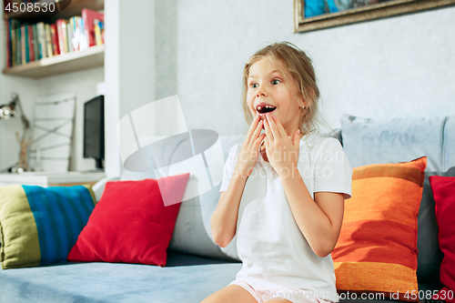 Image of Little surprised teen girl watching tv at home.