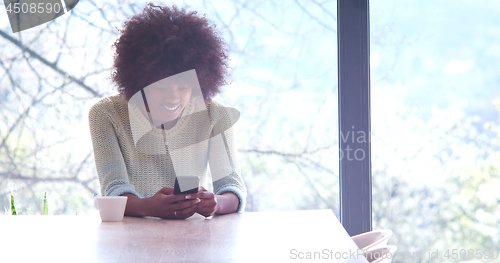 Image of black woman drinking coffee and using a mobile phone  at home