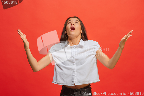 Image of Beautiful female half-length portrait isolated on red studio backgroud. The young emotional surprised woman