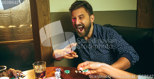 Image of Funny photo of friends sitting at wooden table. Friends having fun while playing board game.