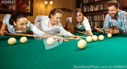 Image of Young men and women playing billiards at office after work.