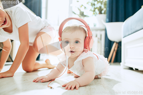 Image of Cute young baby sitting on the floor at home playing with headphones