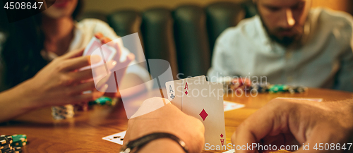 Image of Side view photo of friends sitting at wooden table. Friends having fun while playing board game.