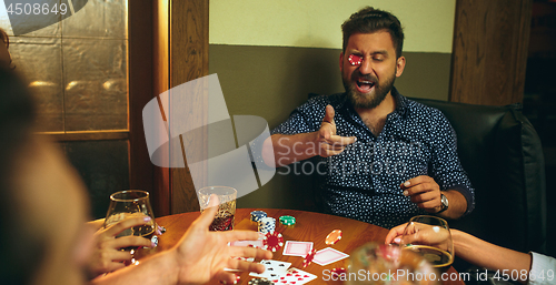 Image of Funny photo of friends sitting at wooden table. Friends having fun while playing board game.