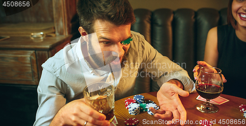 Image of Side view photo of friends sitting at wooden table. Friends having fun while playing board game.