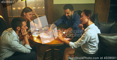 Image of Side view photo of friends sitting at wooden table. Friends having fun while playing board game.