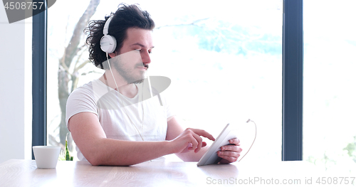 Image of young man listenig music on tablet at home