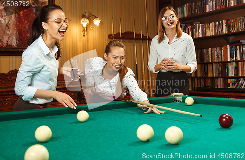 Image of Young women playing billiards at office after work.