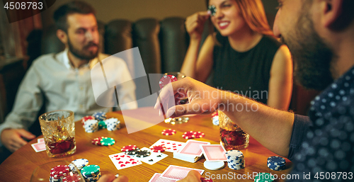 Image of Side view photo of friends sitting at wooden table. Friends having fun while playing board game.