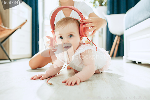 Image of Cute young baby sitting on the floor at home playing with headphones