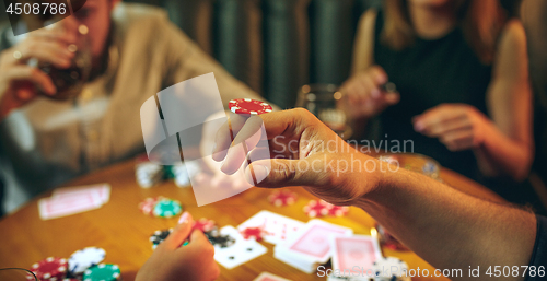 Image of Side view photo of friends sitting at wooden table. Friends having fun while playing board game.