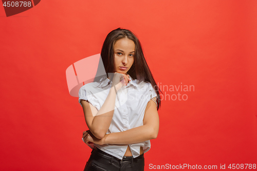 Image of The serious business woman standing and looking at camera against red background.