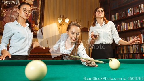 Image of Young women playing billiards at office after work.