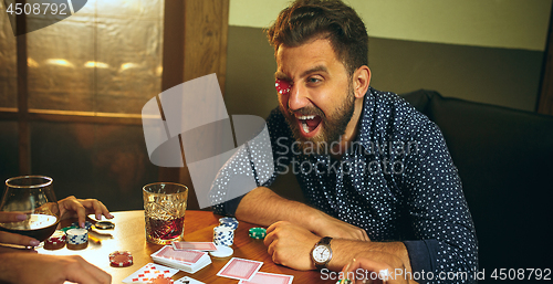 Image of Funny photo of friends sitting at wooden table. Friends having fun while playing board game.