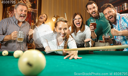 Image of Young men and women playing billiards at office after work.