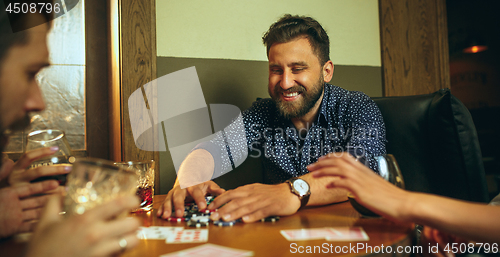 Image of Side view photo of friends sitting at wooden table. Friends having fun while playing board game.