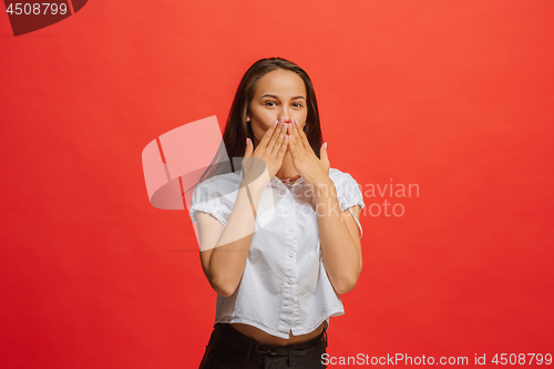 Image of The young woman whispering a secret behind her hand over red background