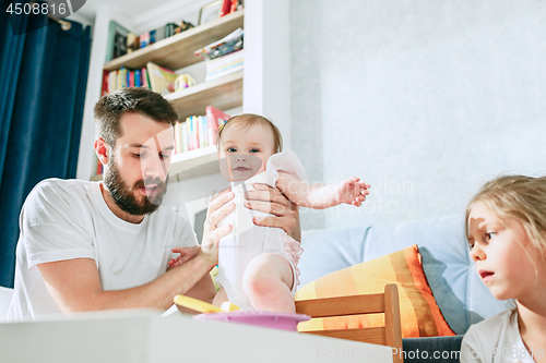 Image of Good looking young man eating breakfast and feeding her baby girl at home