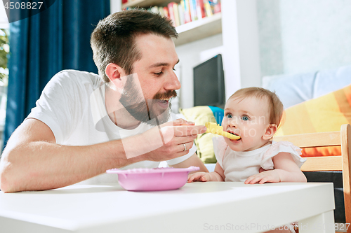 Image of Good looking young man eating breakfast and feeding her baby girl at home