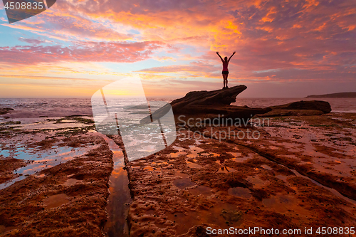 Image of Woman standing on coastal rocks with stunning sunrise and reflec