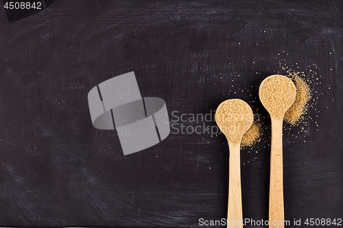 Image of Brown cane sugar in two wooden spoons on black background.