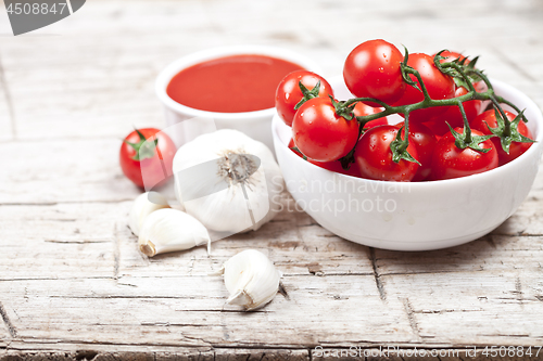 Image of Fresh tomatoes in white bowl, sauce and raw garlic on rustic woo