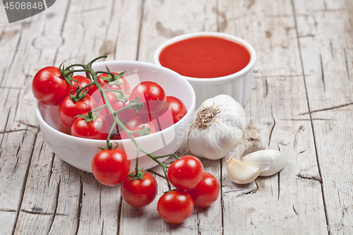 Image of Fresh tomatoes in white bowl, sauce and raw garlic on rustic woo