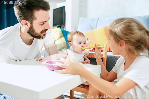Image of Good looking young man eating breakfast and feeding her baby girl at home