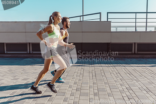 Image of Pretty sporty woman and man jogging at city