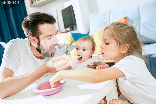Image of Good looking young man eating breakfast and feeding her baby girl at home