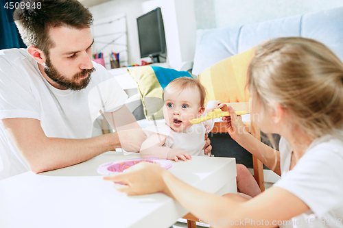 Image of Good looking young man eating breakfast and feeding her baby girl at home