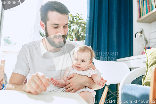Image of Good looking young man eating breakfast and feeding her baby girl at home