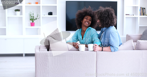 Image of multiethnic couple sitting on sofa at home drinking coffe