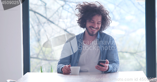 Image of young man drinking coffee and using a mobile phone  at home