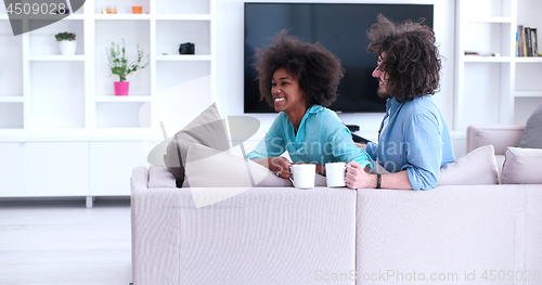 Image of multiethnic couple sitting on sofa at home drinking coffe